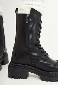Stivali alla caviglia in pelle nera con zip laterale, design lacciato e suola in gomma spessa con bordo testurizzato.