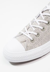 Grå canvas sneakers med vit gummitå och sula, med vita snören och metallöglor. Texturerad tyg med diagonalt mönster.