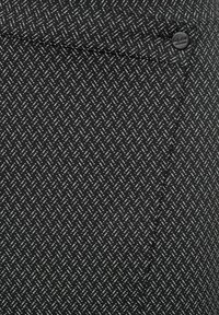 Zwarte stof met een wit geometrisch patroon; heeft een voorste zak en een zwarte knop. De textuur lijkt glad en geweven.