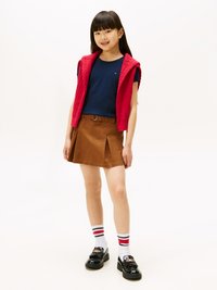 Gonna marrone con pieghe, camicia blu a maniche corte, gilet senza maniche rosso in maglia, scarpe nere e calze bianche con righe rosse.