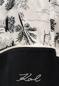 Ύφασμα ασπρόμαυρο με εκτύπωση φοίνικα και τοπίου. Διαθέτει κεντημένο λογότυπο σε λευκό. Ο σχεδιασμός περιλαμβάνει αντιθετικά περιθώρια.