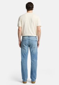 Jeans in denim azzurro chiaro con taglio dritto, caratterizzati da vita media, tasche posteriori e una t-shirt beige a maniche corte.
