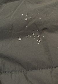 Tessuto nero resistente all'acqua con una texture opaca, caratterizzato da piccole gocce d'acqua sulla superficie e linee di cucitura visibili.