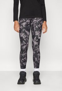 Sort langærmet top med leggings, der har et mørkegråt og lyslilla abstrakt mønster; båret med sorte vandresko og hvide sokker.
