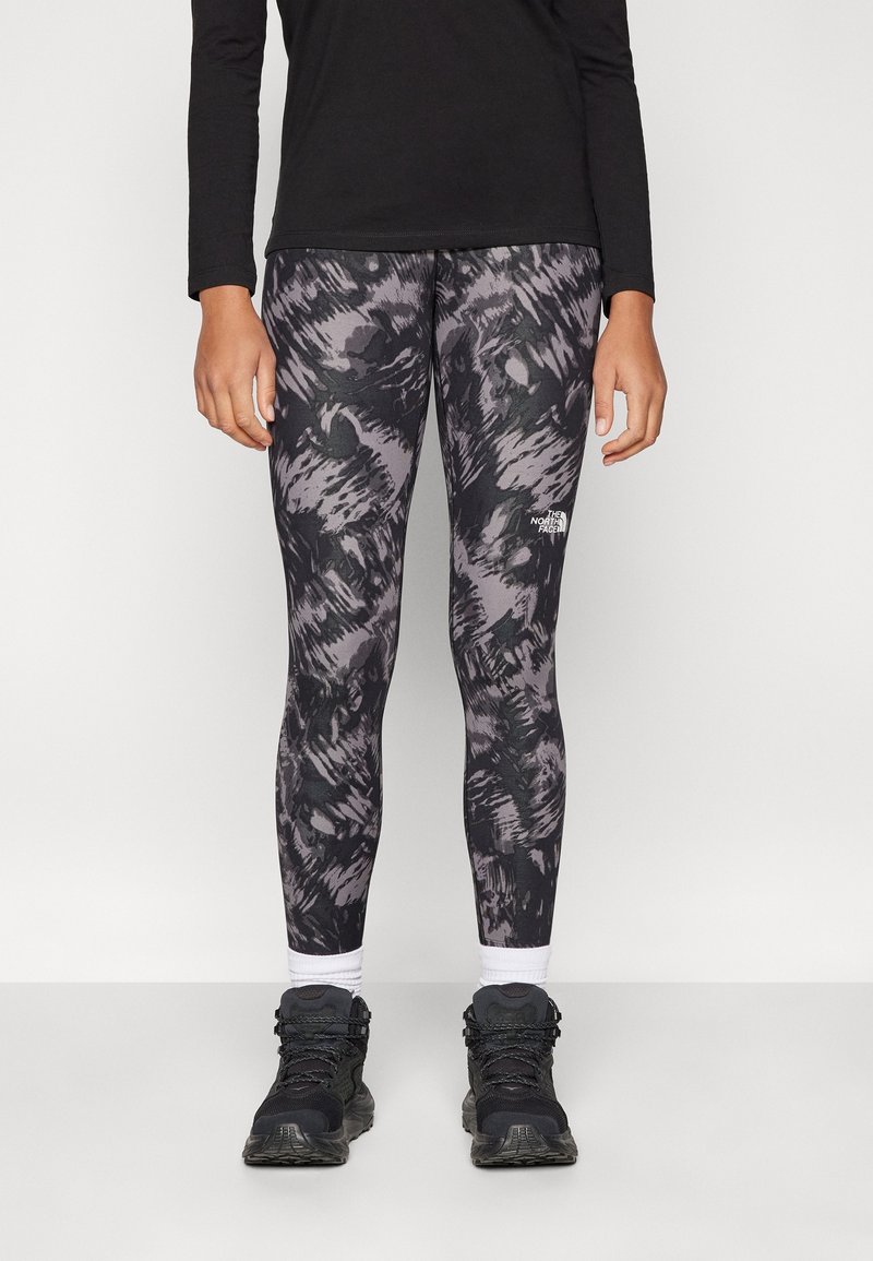 Sort langærmet top med leggings, der har et mørkegråt og lyslilla abstrakt mønster; båret med sorte vandresko og hvide sokker.