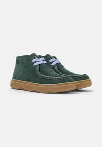 Botas de ante verdes hasta el tobillo con cordones azul claro y suelas de goma marrón, presentadas sobre un fondo blanco liso.