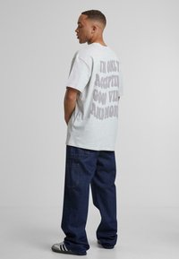 T-shirt grise surdimensionnée avec du texte en relief audacieux au dos. Associé à un pantalon en denim foncé et des baskets noir et blanc.
