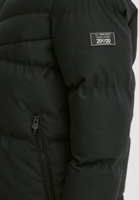 Sort puffersk Jacket med quiltet design, der har en lynlåslomme og et logo-patch på venstre ærme. Glat tekstur, letvægtsmateriale.
