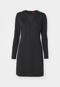 Černé šaty s dlouhým rukávem a hlubokým výstřihem do V, s texturovaným panelem na hrudi a zapínáním na zip na zádech. Hladký povrch látky.