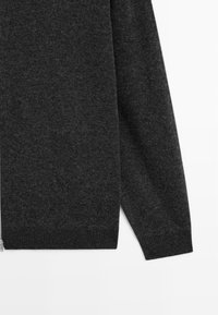 Maglione grigio scuro con zip, realizzato in tessuto morbido. Presenta una texture liscia e polsini a coste, con una silhouette dritta e dettagli minimi.