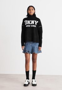 Svart stickad tröja med texten "DKNY NEW YORK", ihop med en denimbaserad utsvängd kjol. Svarta strumpor och vita skor fulländar outfiten.