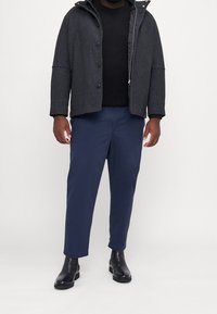 Dunkelgraue Wollmischung Jacke mit Reißverschluss und Knöpfen, kombiniert mit navyfarbigen Hosen und schwarzen Lederstiefeletten. Darunter ein strukturiertes Strickoberteil.