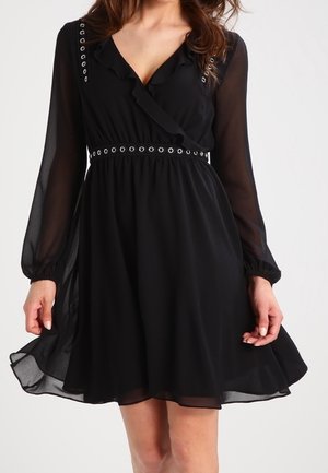 Czarna sukienka do kolan z przezroczystymi długimi rękawami, falbankowanym dekoltem w kształcie litery V oraz metalicznymi oczkami na ramionach i w talii.
