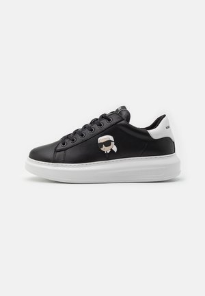 Baskets en cuir noir avec une semelle blanche, présentant un design de bande dessinée sur le côté, des lacets ronds, et un logo sur le talon et la languette.
