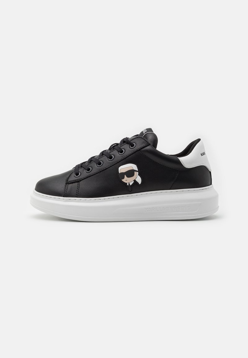 Zwarte leren sneakers met een witte zool, voorzien van een cartoonontwerp aan de zijkant, ronde veters en merklogo op de hiel en tong.