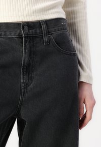 Black denim jeans with a high waist, front pockets, and subtle stitching details. The texture is smooth with a slight stretch.