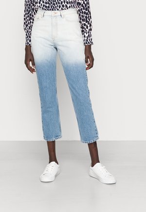 Personne portant un jean taille haute, coupe droite, avec un dégradé ombré bleu allant de blanc en haut à bleu clair en bas, associé à des baskets blanches.