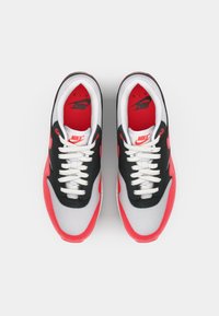 Adidași cu un design în nuanțe de negru, gri și roșu; material superior din plasă cu accente din piele întoarsă; șireturi albe; brandingul iconic Nike pe limbă.