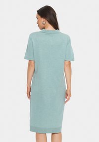 Világoskék kötött ruha polo gallérral, rövid ujjal és bordás szegéllyel. Az anyag lágynek tűnik, és kényelmes illeszkedést biztosít.