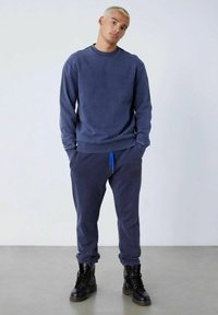 Sudadera azul marino con puños y dobladillo acanalados, combinada con joggers a juego que presentan un cordón azul y un detalle de logo texturizado. Botas negras.