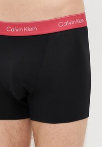 Mustat bokserishortsit, joissa on punainen vyötärönauha ja valkoinen "Calvin Klein" -logo. Sileä kangas ja istuva malli.