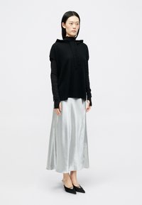 Μαύρο φούτερ με κουκούλα, μακριά μανίκια από κάτω, συνδυασμένο με μια ρέουσα ασημί σατέν φούστα και μαύρες μυτερές στιλέτο. Λείοι υφές, μινιμαλιστικός σχεδιασμός.