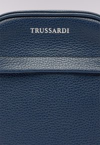 Borsa in pelle blu navy con texture e parte superiore liscia. Presenta un logo "TRUSSARDI" in argento e dettagli di fine cucitura.