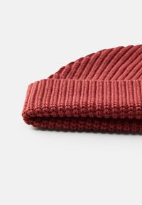 Strik-hat i mørkerød med ribbet tekstur og en foldet mansjetdesign. Materialet virker blødt og varmt.
