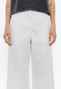Pantalones de pierna ancha blancos con una textura suave y costuras laterales que bajan por el frente, combinados con un top corto gris oscuro.