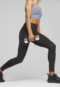 Leggings sportivi neri con pannelli in rete, abbinati a un reggiseno sportivo azzurro chiaro. La persona tiene in mano pesi in argento mentre si trova in posizione di affondo.