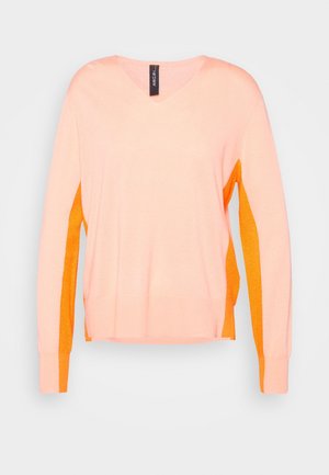 Pull pêche à manches longues avec panneaux latéraux orange et poignets assortis, col en V, et une étiquette de marque noire au niveau du col sur un fond uni.