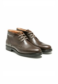 Une paire de bottes en cuir marron à lacets, à bouts ronds et semelles noires présentée sur un fond blanc.