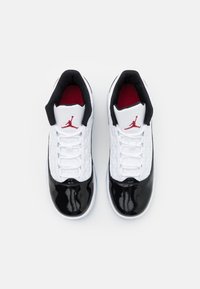 Bílé basketbalové boty s černou lakovanou špičkou, síťovanými bočními panely, červenými akcenty uvnitř a výrazným logo Jumpman na jazyku.