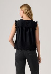 Blusa nera senza maniche con rifiniture in pizzo e orlo a onde, caratterizzata da una schiena arricciata e chiusura a bottoni sulla scollatura. Tessuto testurizzato.