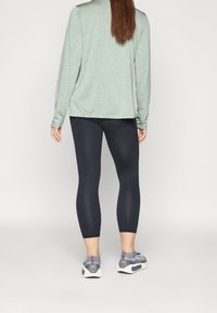 Pitkähihaisen vaaleanvihreän paidan, mustien leggingsien ja harmaiden urheilukenksien yhdistelmä. Paita on rentoa tyyliä; kangas vaikuttaa pehmeältä ja siinä on heather-kuitutekstuuri.