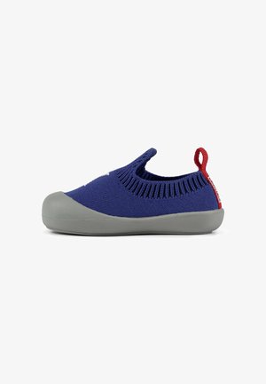 Zapato infantil con parte superior de punto elástico en azul marino y suela de goma gris. Cuenta con una lengüeta roja en el talón. Punta redondeada y diseño sin cordones.