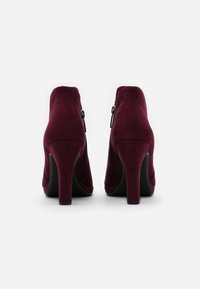 Burgundy suede high-heeled ankle boots with a zipper detail on the outer side, featuring a tapered heel and smooth texture.