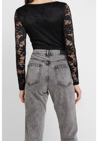 Top lungo a maniche a rete nera con motivo floreale, abbinato a jeans in denim grigi a vita alta con una trama sbiadita e tasche posteriori.