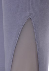 Purple legging featuring a cut-out detail with sheer mesh underneath. Smooth fabric with a textured seam along the edge.