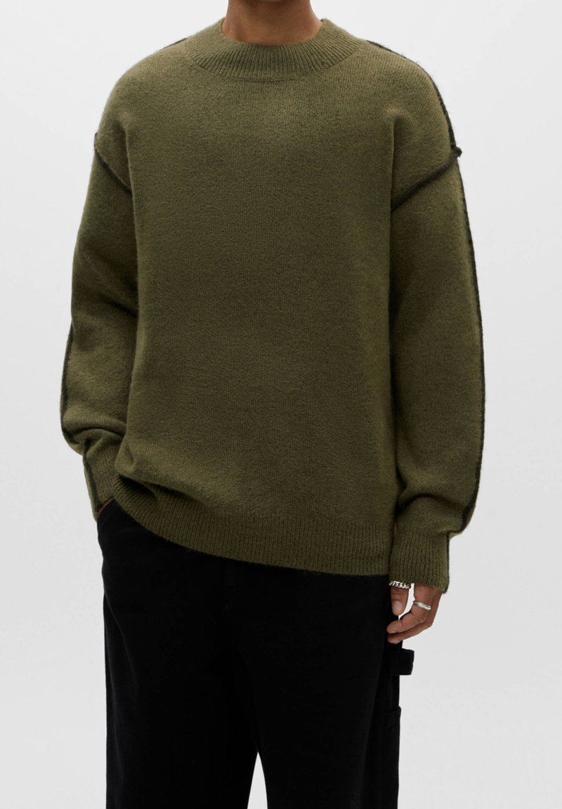 Khaki zielony sweter dziany z okrągłym dekoltem, opadłymi ramionami i prążkowanymi mankietami. Miękka tekstura, luźny krój i kontrastowe detale szycia.