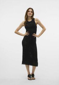 Černé pletené midi šaty s bezramínkovým designem, geometrickými vzory a vykrojeným lemem. Kombinované s černými sandály.