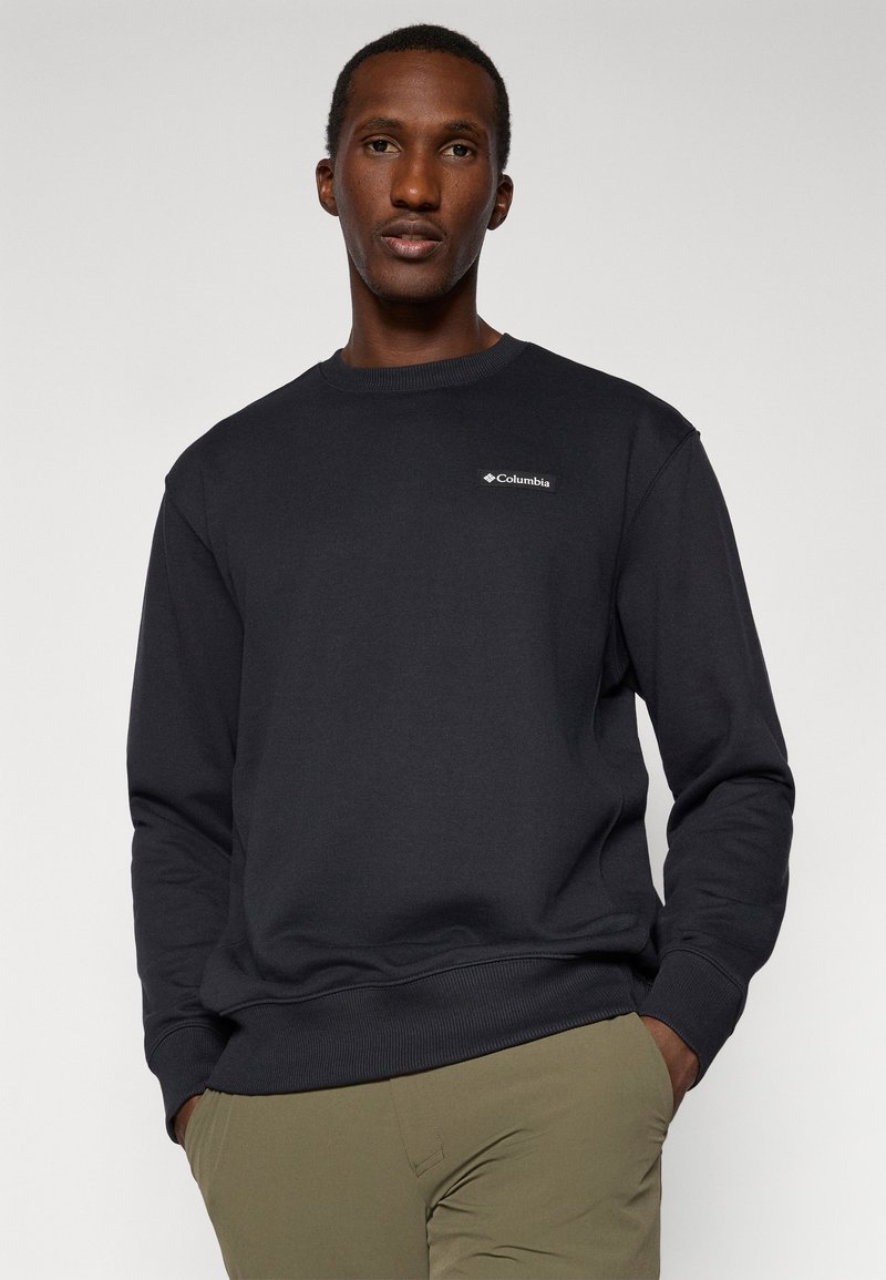 Sweatshirt noir à col rond en tissu mélangé coton. Présente un petit logo blanc Columbia sur la poitrine et des poignets et un ourlet côtelés.