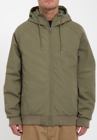 Olijfgroene hoodie met een voorzijde rits, ribbelmanchetten en -tailleband. Heeft een subtiel logo en een gladde textuur.