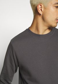 Grå sweatshirt med mankohals, laget av mykt stoff, med en subtil tekstur og tilpassede ermer, som fremhever et minimalistsk design.
