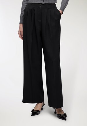 Pantaloni neri a gamba larga con vita alta, pieghe e due tasche frontali. Il materiale appare liscio con un design strutturato.