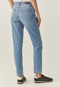 Jeans din denim de un albastru deschis, cu o croială slim, prezentând două buzunare la spate cu cusături vizibile și o etichetă din piele maro la talie.