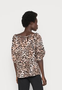 Blusa com padrão de leopardo em tons de castanho e bege, com mangas bufantes e um decote em gota nas costas com fecho de atar. Textura de tecido suave.
