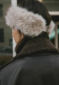 Faux furørepropper i lys grå farve med et tykt bånd; båret med en mørkebrun, tekstureret shearlingkravejakke.