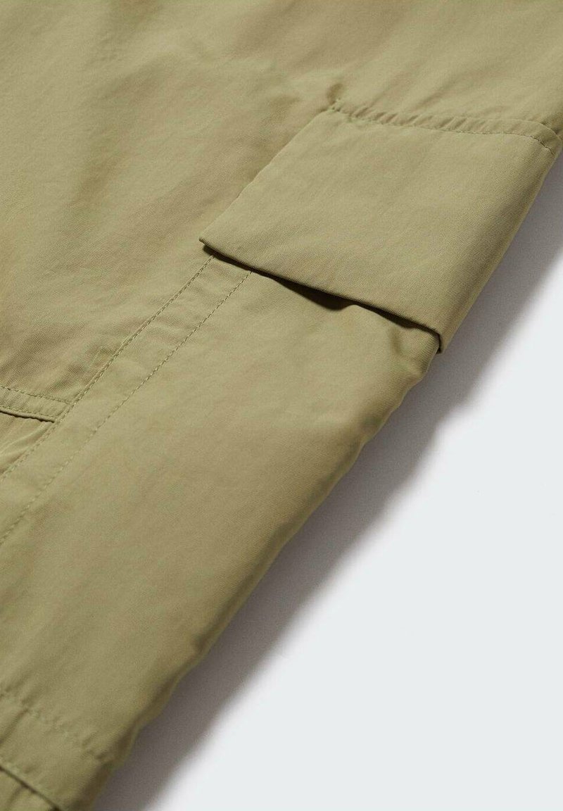 Jasnooliwkowa rękaw kurtki z złożonym mankietem, gładka tekstura i widoczne szwy, prezentująca minimalistyczny design.