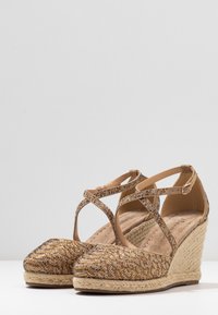 Sandalias tipo cuña en dorado y marrón con correas entrecruzadas, parte superior de tejido texturizado y media suela envuelta en yute. Diseño de punta cerrada.